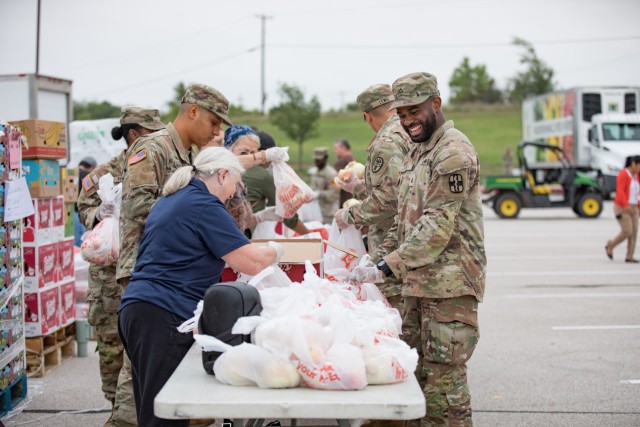 People stand on both sides of a long row of tables filled with plastic bags.