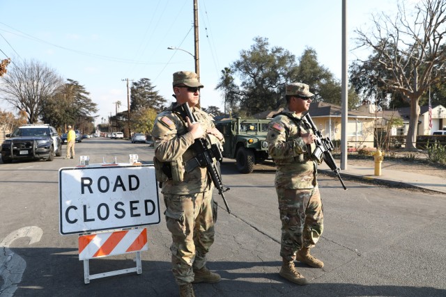 U.S. Army Sgt. Jacen Ramos and Pfc. Matthew Mechelin, cannon crewmembers with 1st Battalion, 143rd Field Artillery Regiment, 79th Infantry Brigade Combat Team, California Army National Guard, stand guard at a traffic control point near the Eaton...