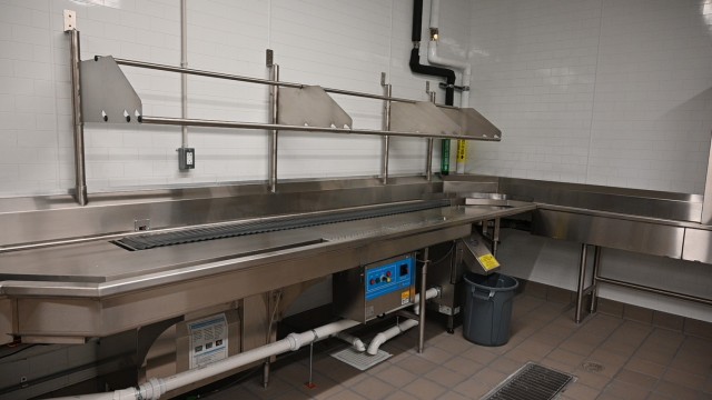 An empty, clean, stainless steel table sits against a wall.