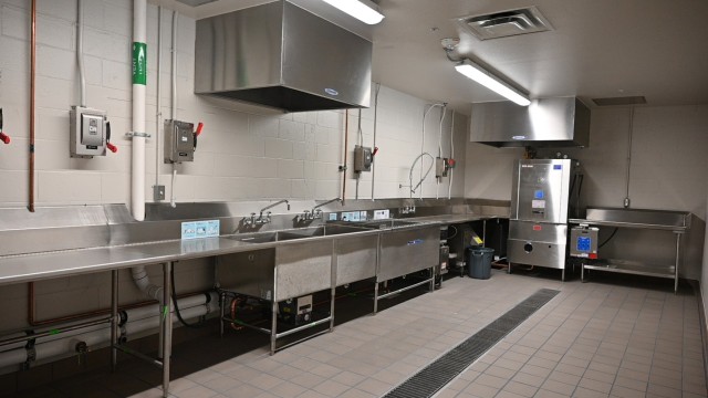 An open, industrial kitchen with stainless steel appliances sit.