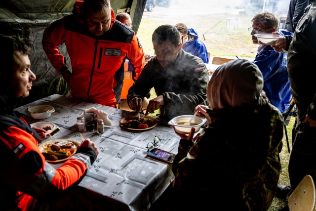 Polish Soldiers and medical personnel gather under a tent to share a hot meal following an emergency services exercise in Powidz, Poland, May 15, 2024. The joint training event brought together military and civilian responders to strengthen...
