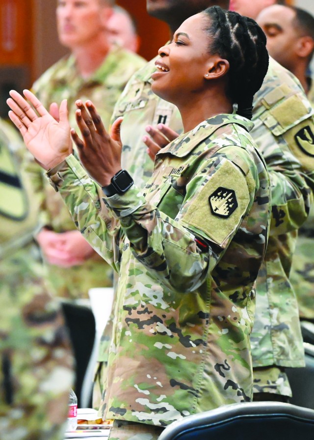 A woman standing holds hands up in front of her with elbows bent and palms facing inside, her mouth open and eyes closed.
