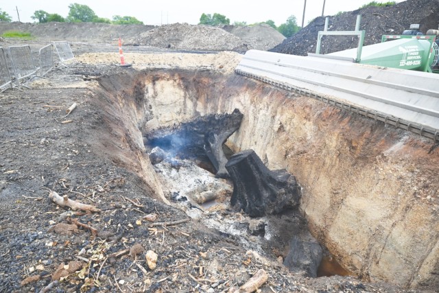 The embers of burnt tree stumps and parts smoke in a trench recessed in the ground.