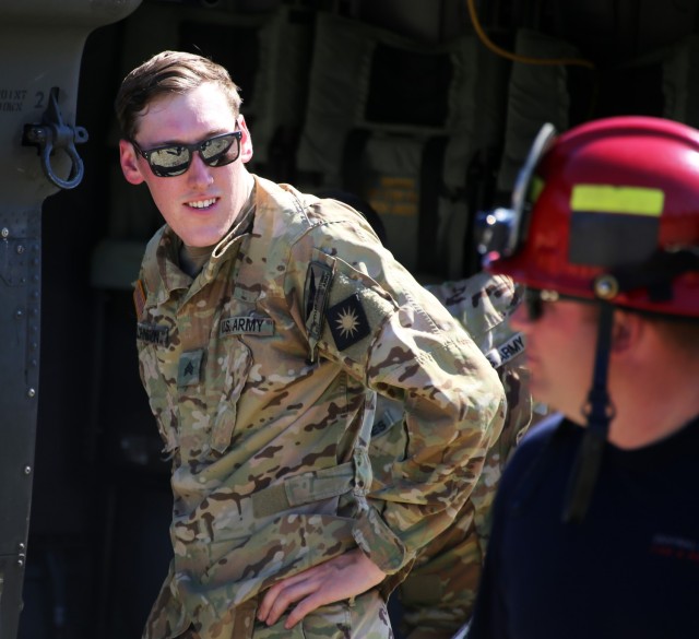Sgt. Tyler Johnston, Crew Chief, Charlie Company, 1st Battalion, 140th Aviation, 96th Aviation Troop Command, talks with firefighters from Central Pierce Fire and Rescue prior to water bucket training, June 30, 2025 near Puyallup, Wash.