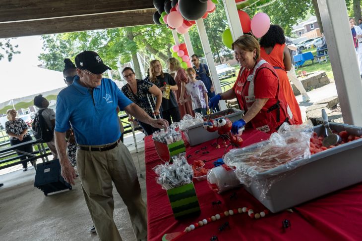 Volunteer hands out watermelon to a man.
