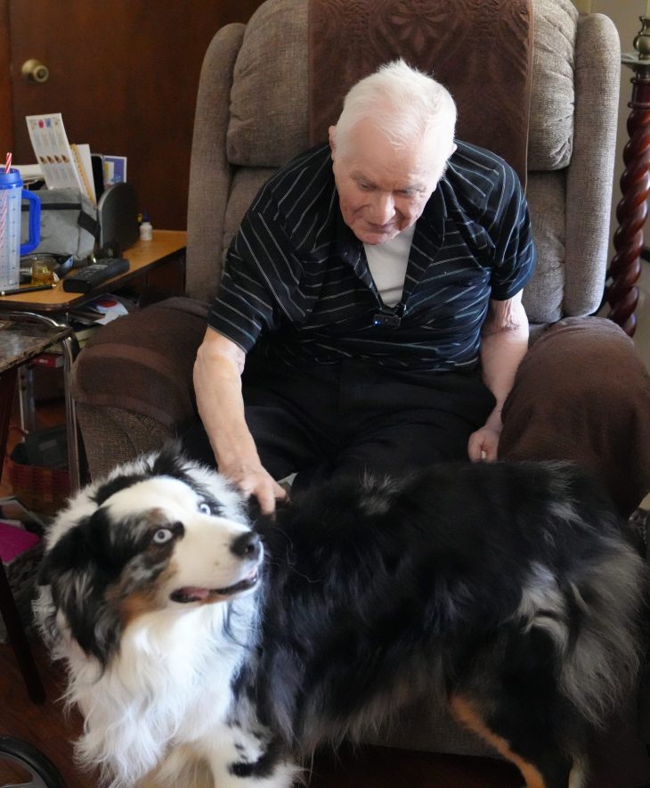 Man sitting in a recliner pets a black and white dog.